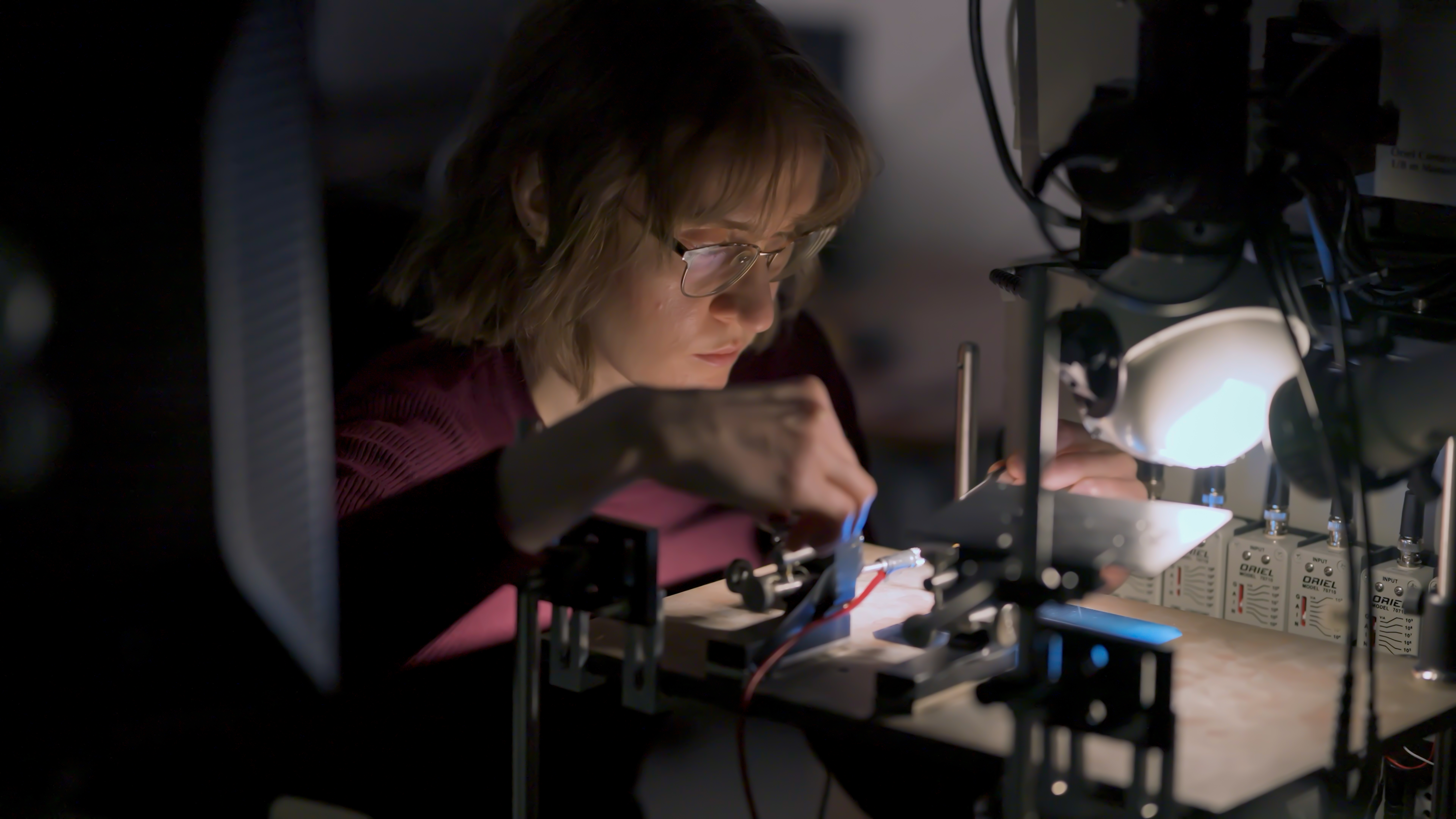 A dramatic photo of a University of Ottawa research student in a dark room with a spotlight on her work.