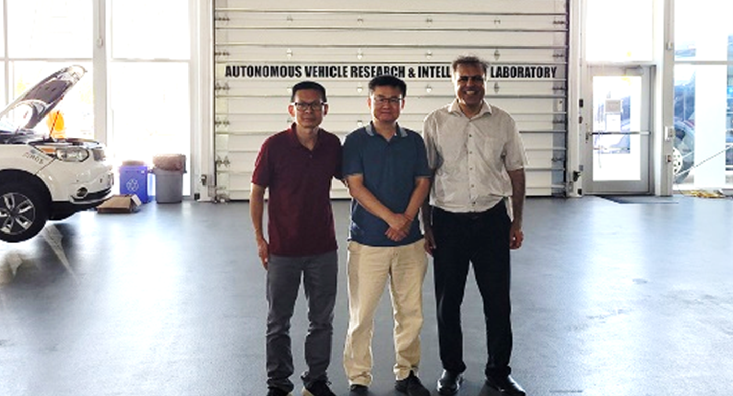 Members of the research team at the Autonomous Vehicle Lab stand together in a warehouse, facing the camera and smiling.